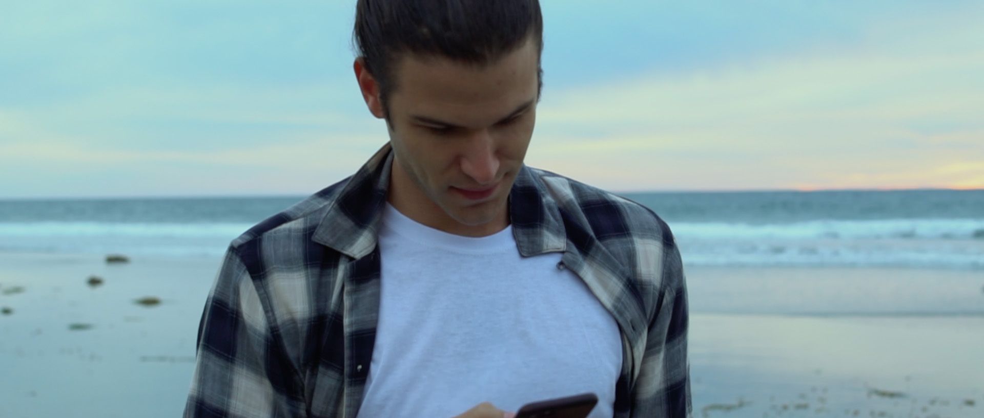 A still of JJ walking on the beach looking at his phone.